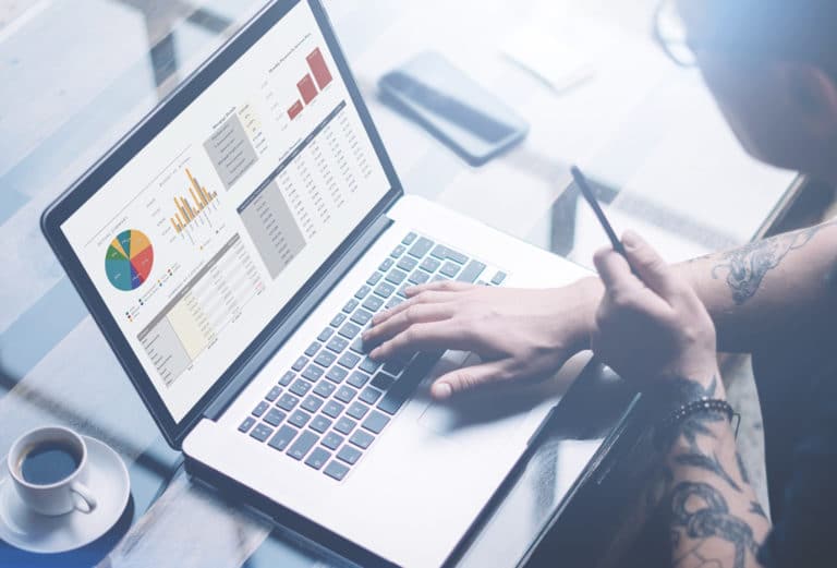 A person looking at financial graphs while investing on their laptop.